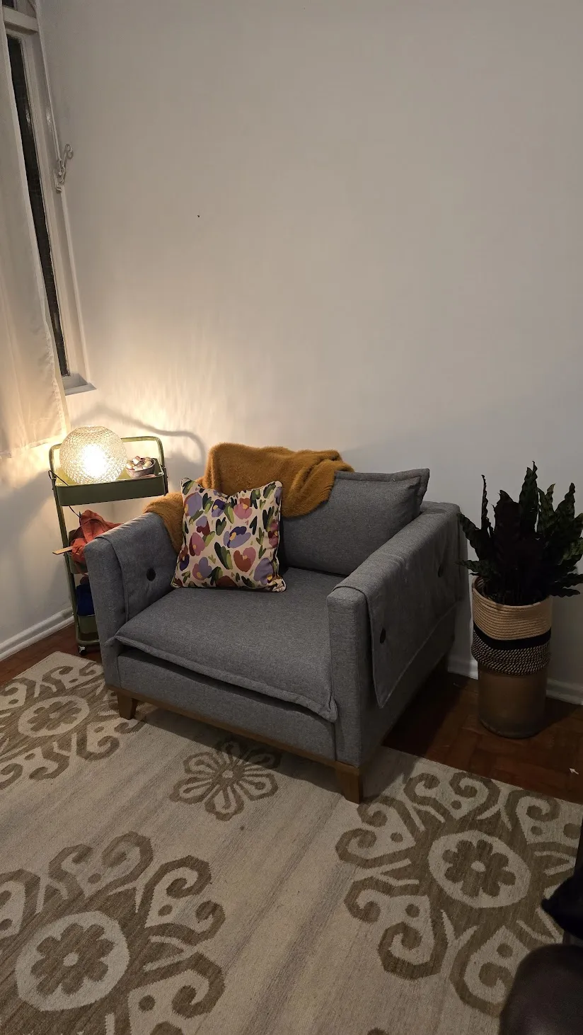 Sala do consultório com sofá cinza, almofadas, tapete estampado e luminária acesa